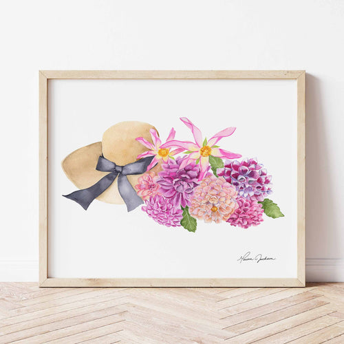 tan sunhat with black bow beside a bunch of pink, coral, fuscia, and purple dahlias with green leaves