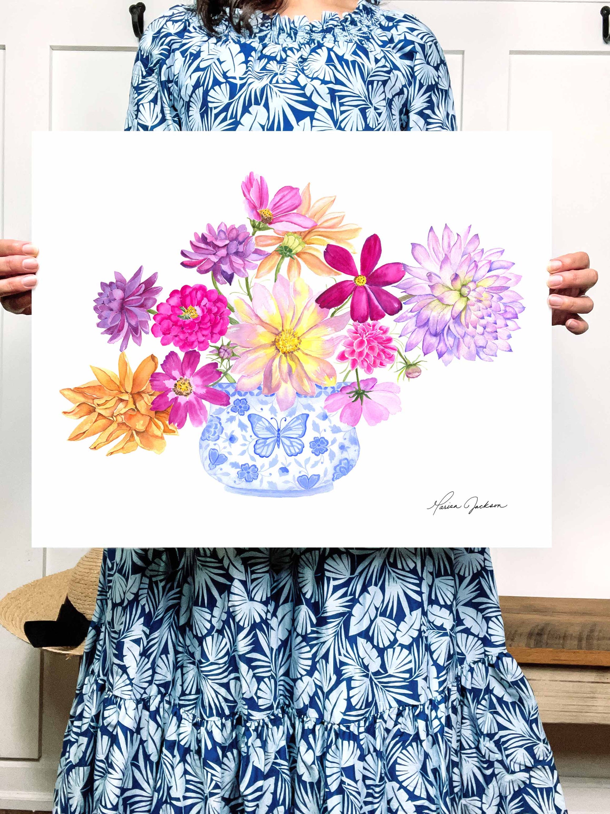woman holding picture of Blue and White vase filled with bright dahlia flowers of different varieties. Colors used: purple, lilac, magenta, pink, yellow, royal blue, light blue, orange